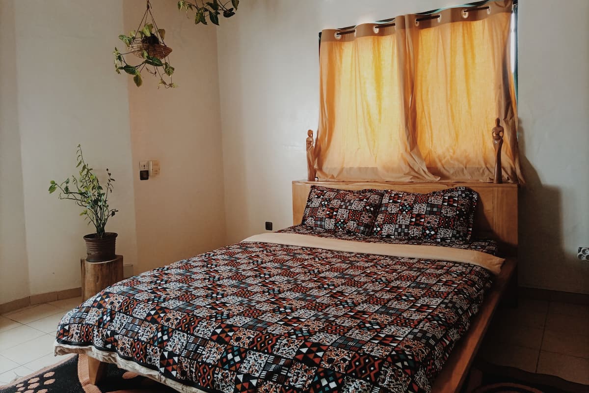 A bedroom with a wooden bed, patterned bedding, a potted plant, and a ceiling fan.