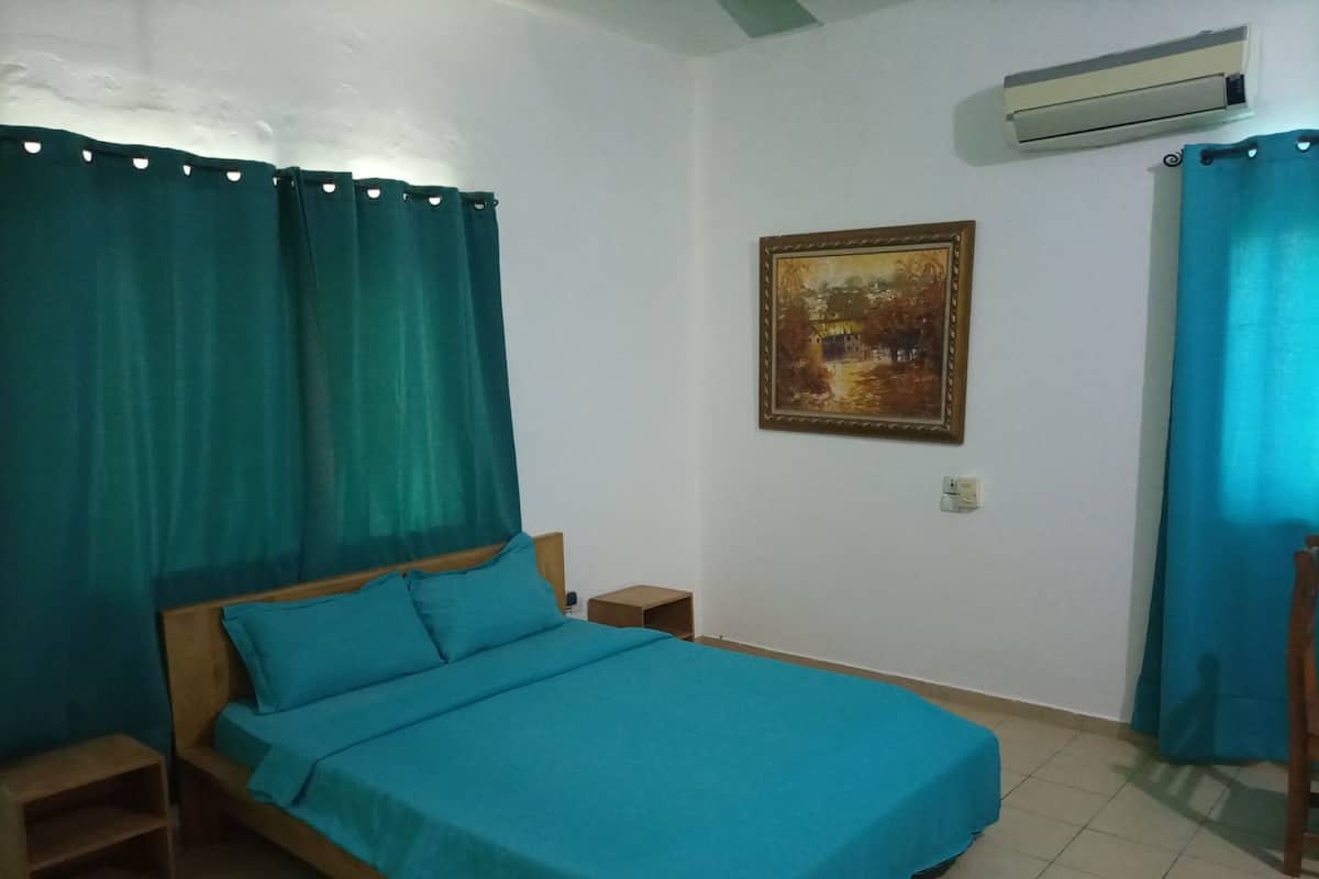 A bedroom with a bed, a nightstand, an air conditioner, and a painting on the wall.