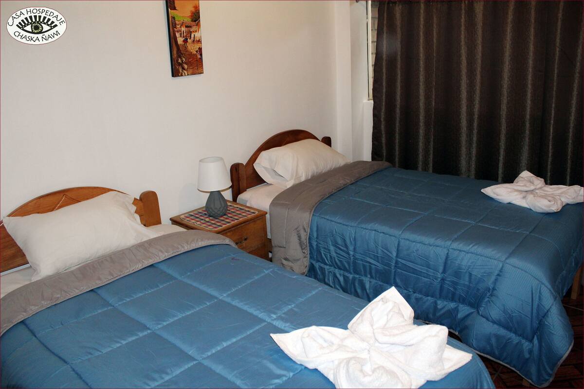 A hotel room with two beds, a nightstand with a lamp, and a painting on the wall.