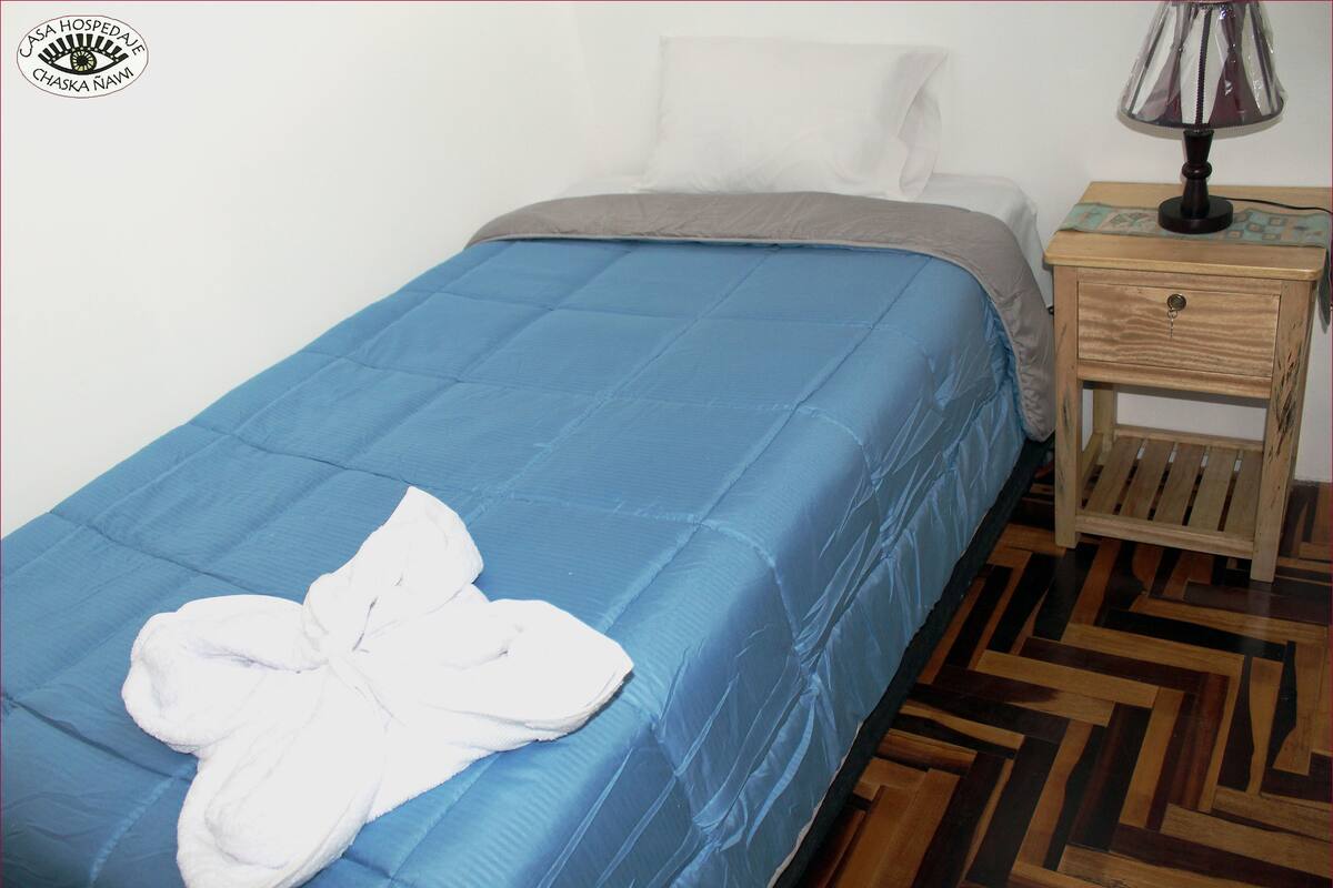 A neatly made bed with a blue bedspread and a white towel folded on it.