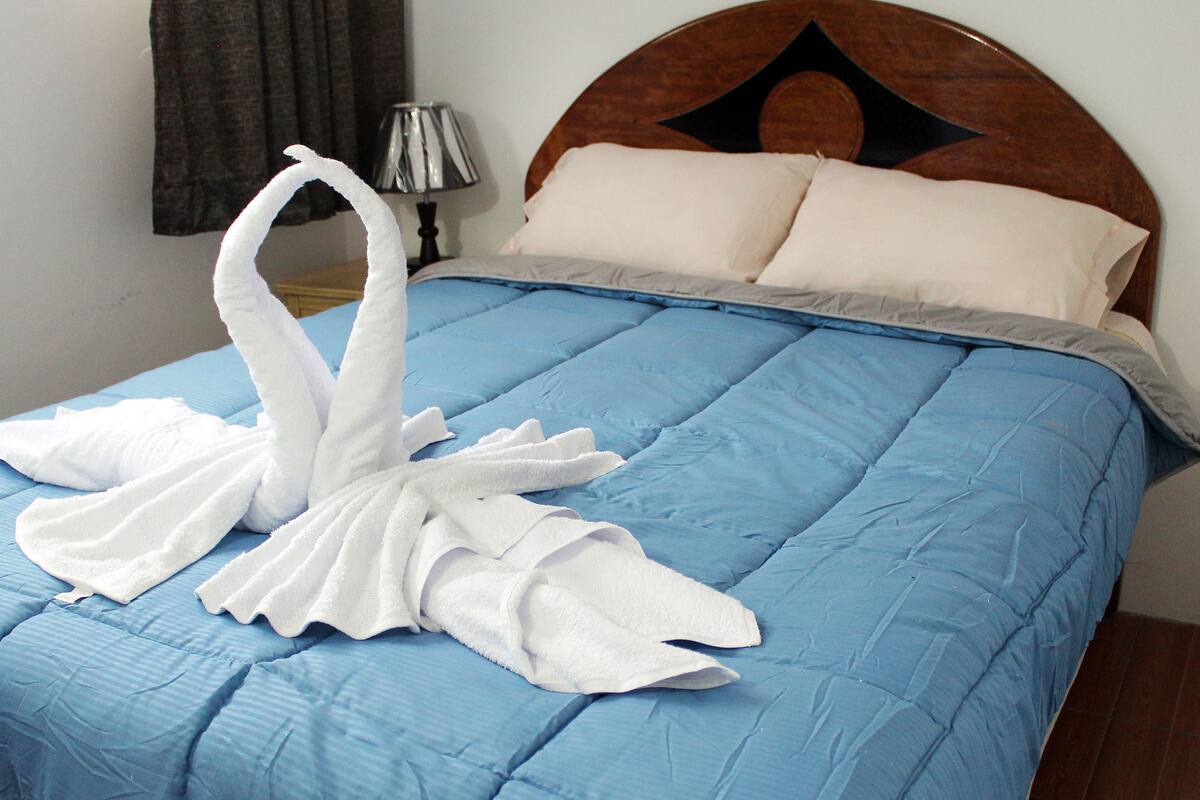 A bed with a blue quilt, a wooden headboard, and a lamp on a bedside table.