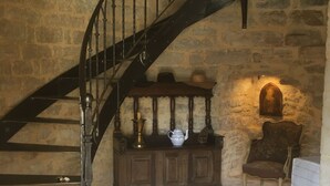 A stone-walled room with a spiral staircase, a wooden cabinet with decorative items, and a chair. - Chambres d'hôtes La Tour de Ginaillac (Les Arques)