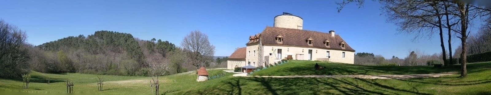 Un bâtiment historique doté d’une tour ronde, entouré d’un paysage verdoyant et luxuriant ainsi que d’arbres.