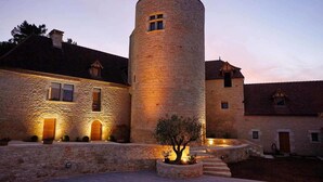 A stone building with a cylindrical tower, multiple windows, and a well-lit entrance. - Chambres d'hôtes La Tour de Ginaillac (Les Arques)