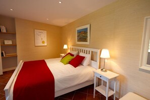 A neatly made bed with a red blanket and pillows, a bedside table with a lamp, and a framed picture on the wall. - Chambres d'hôtes La Tour de Ginaillac (Les Arques)