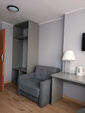 A room with a grey sofa, a desk with a lamp, a kettle, and a wardrobe. - Hotel Pomorski (Bydgoszcz)