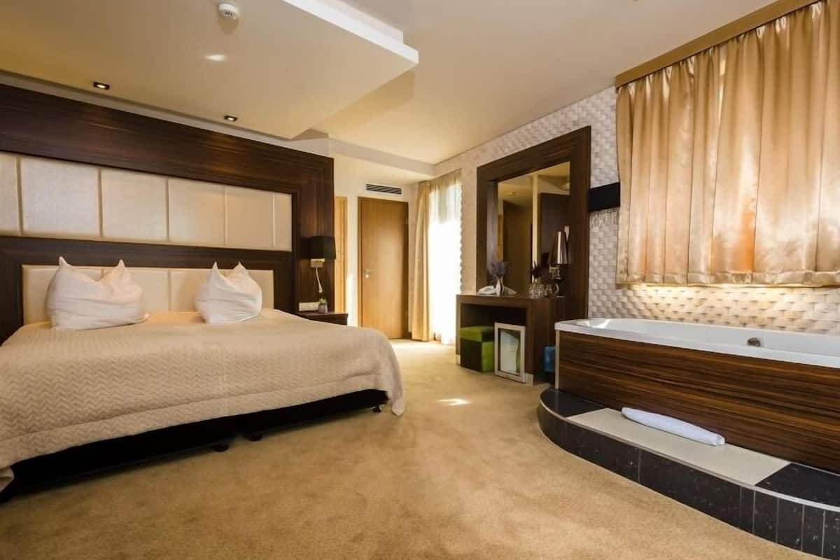 Une chambre d’hôtel avec un grand lit, une salle de bain séparée avec une baignoire et un miroir au-dessus du lavabo.