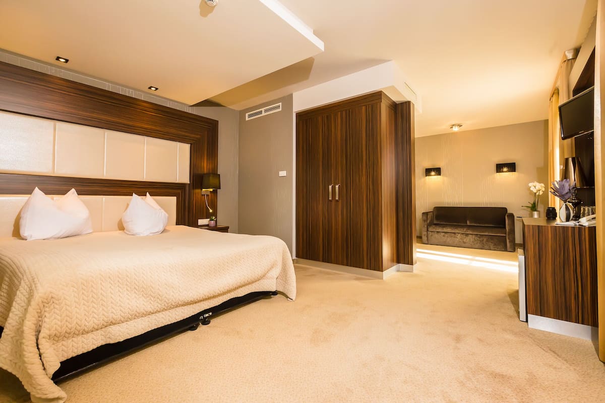 Une chambre d’hôtel comprenant un lit, une armoire en bois, un canapé et un bureau avec une lampe et un vase de fleurs.