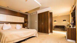 Habitación de hotel con cama, armario de madera, sofá y escritorio con lámpara y un florero con flores.