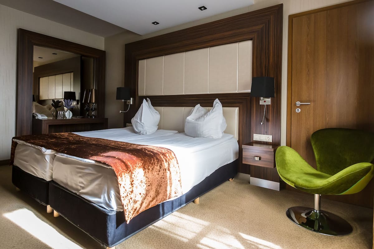 Une chambre d’hôtel avec un grand lit, un fauteuil vert, une porte en bois et un miroir.