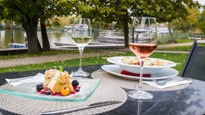 Una mesa con una copa de vino blanco y una copa de vino rosado, un plato con comida a la parrilla y un postre con bayas.