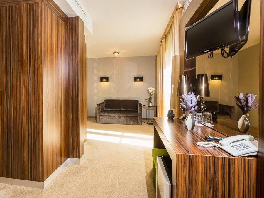 Ein Hotelzimmer mit Holzschrank, einer Couch, einem Fernseher, einem Schreibtisch mit Telefon und einem Spiegel.