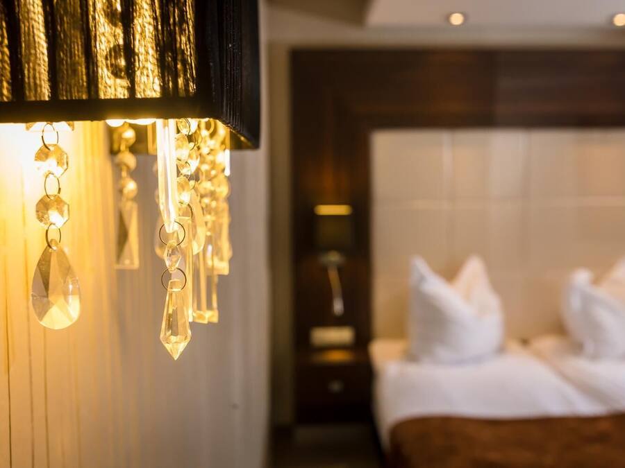 A hotel room with a bed, white pillows, and a wall-mounted light fixture.