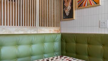 Un asiento tapizado verde con una mesa estampada, listones de madera y una obra de arte radial de colores en la pared.