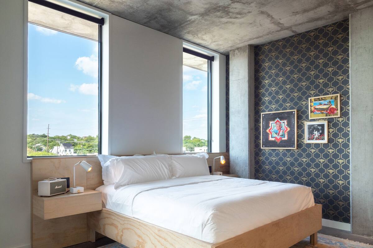 Une chambre à coucher avec un lit, des tables de chevet, une lampe et une vue sur l’extérieur.