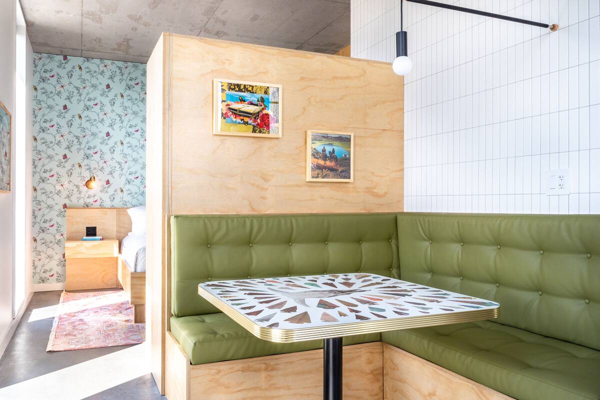 Un intérieur moderne avec un banc rembourré de couleur verte, une petite table ornée d’un motif géométrique et deux œuvres d’art encadrées accrochées au mur.