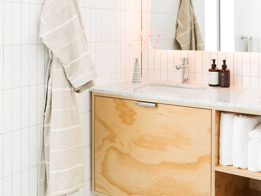 Un baño con pared de azulejos blancos, un tocador de madera con espejo y un perchero para toallas.