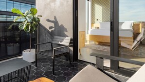 Ein modernes Hotelzimmer mit einem großen Bett, einem kleinen Schreibtisch und einem Balkon mit einem Blumentopf.