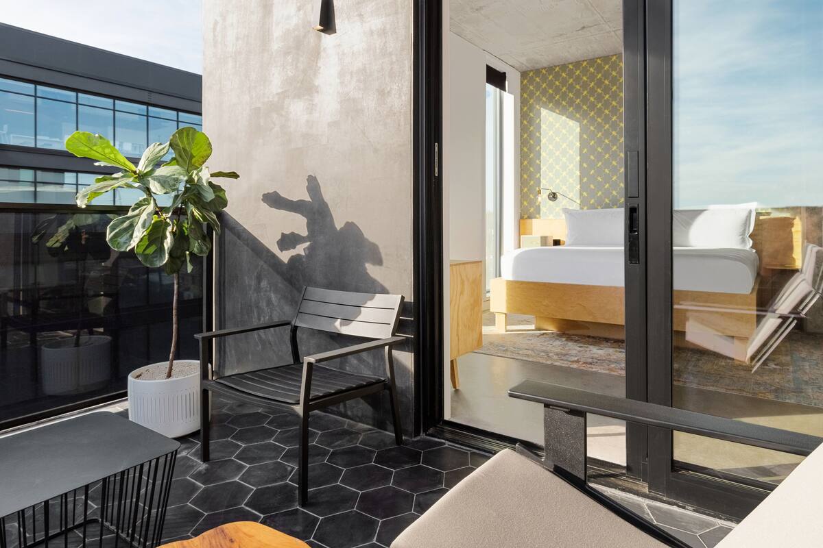Une chambre d’hôtel moderne avec un grand lit, un petit bureau et un balcon agrémenté d’une plante en pot.