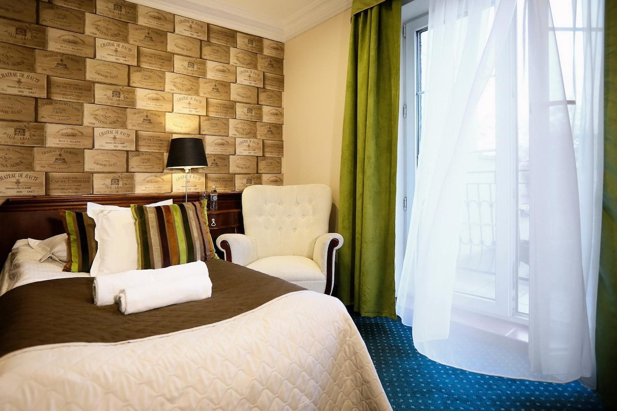 A hotel room with a bed, a chair, a nightstand, and a wall of vintage-style plaques.