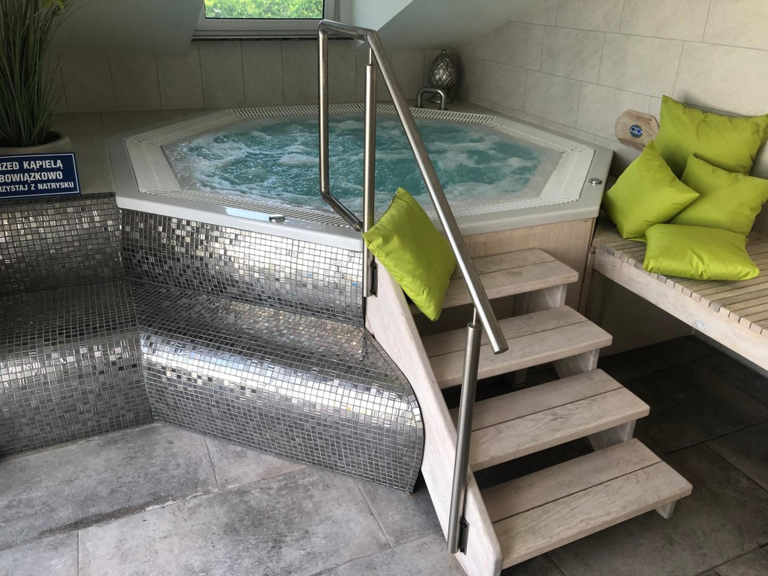 A hot tub with steps leading up to it, a bench with cushions, and a sign in Polish.
