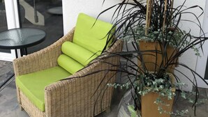 A wicker chair with a green cushion, a life preserver with 'MOËT' on it, and a tall plant in a wooden pot.