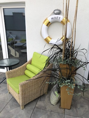 A wicker chair with a green cushion, a life preserver with 'MOËT' on it, and a tall plant in a wooden pot.