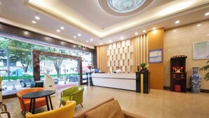 A hotel lobby with a reception desk, seating area, and a large window offering a view of the street.