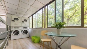 A laundry room with stacked washing machines, a glass table with a potted plant, and chairs.
