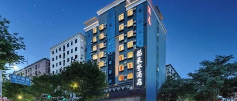 A multi-story hotel with a modern facade, illuminated signage, and a prominent entrance at street level.