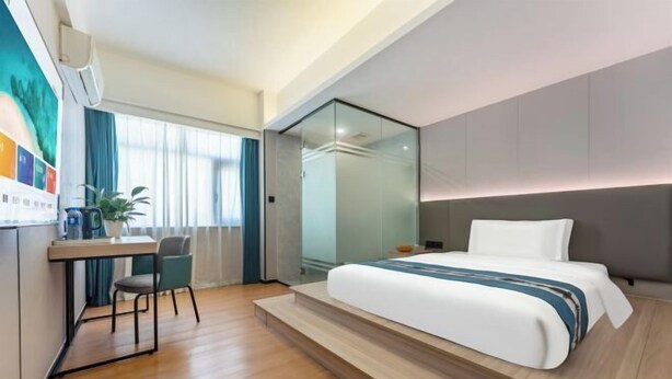 A modern hotel room with a bed, desk, chair, and a glass partition.