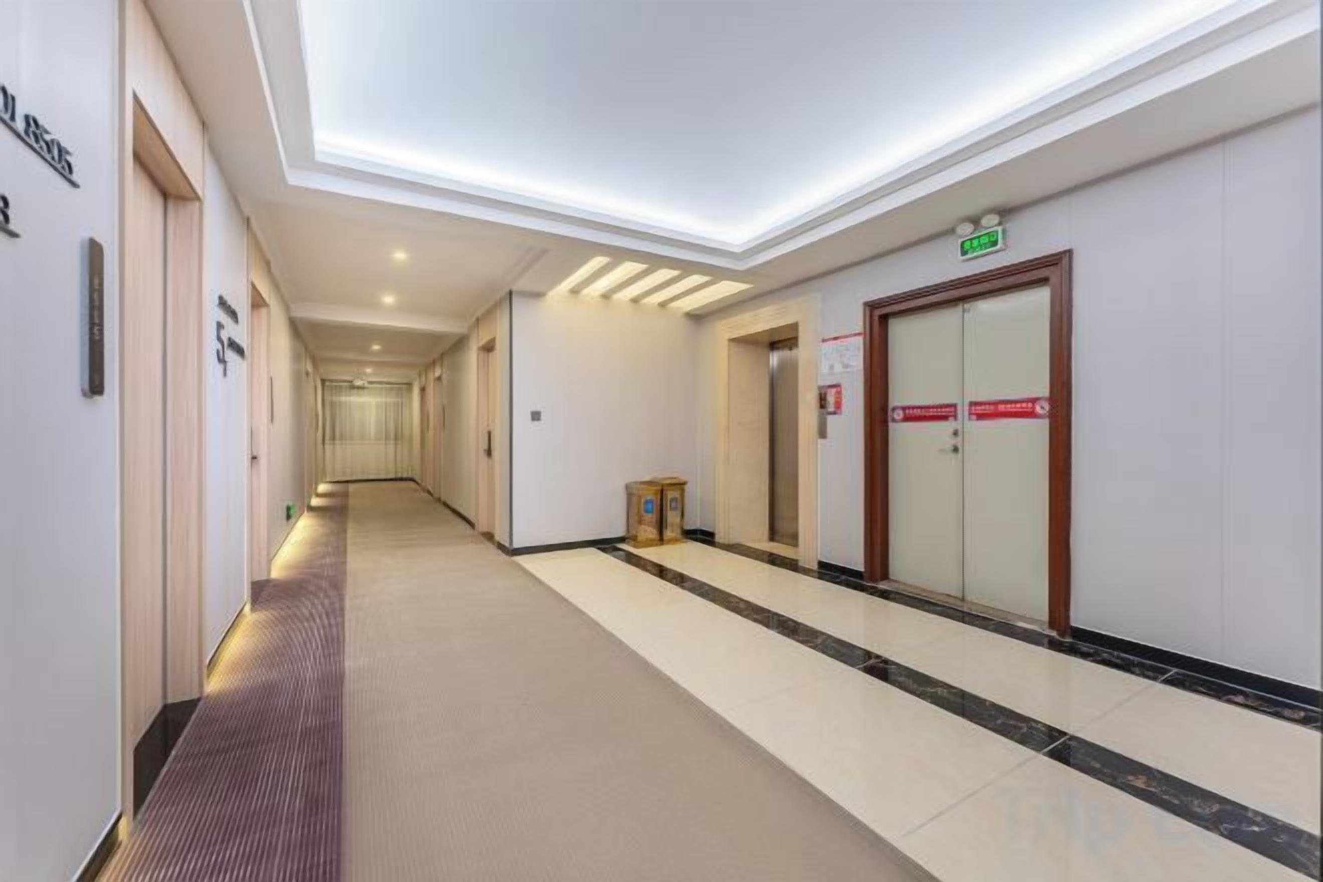 Un pasillo de hotel con piso alfombrado, una puerta de madera y una señal que indica el camino al ascensor.