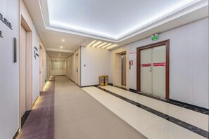 Passadís d'hotel amb sòl de moqueta, una porta de fusta i un senyal que indica el camí cap a l'ascensor.