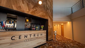 Een hotel lobby met een houten receptiebalie, waarop 'CENTRUM HOTEL' staat, en een bar met verschillende flessen.