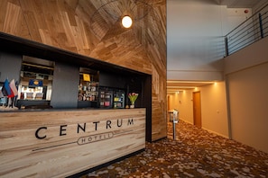 A hotel lobby with a wooden reception desk labeled 'CENTRUM HOTEL' and a bar area with various bottles.