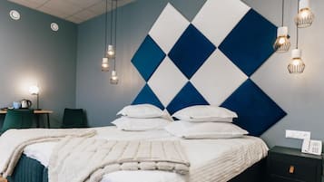 A modern bedroom with a large bed, multiple pillows, a bedside table with a lamp, and a wall-mounted phone.