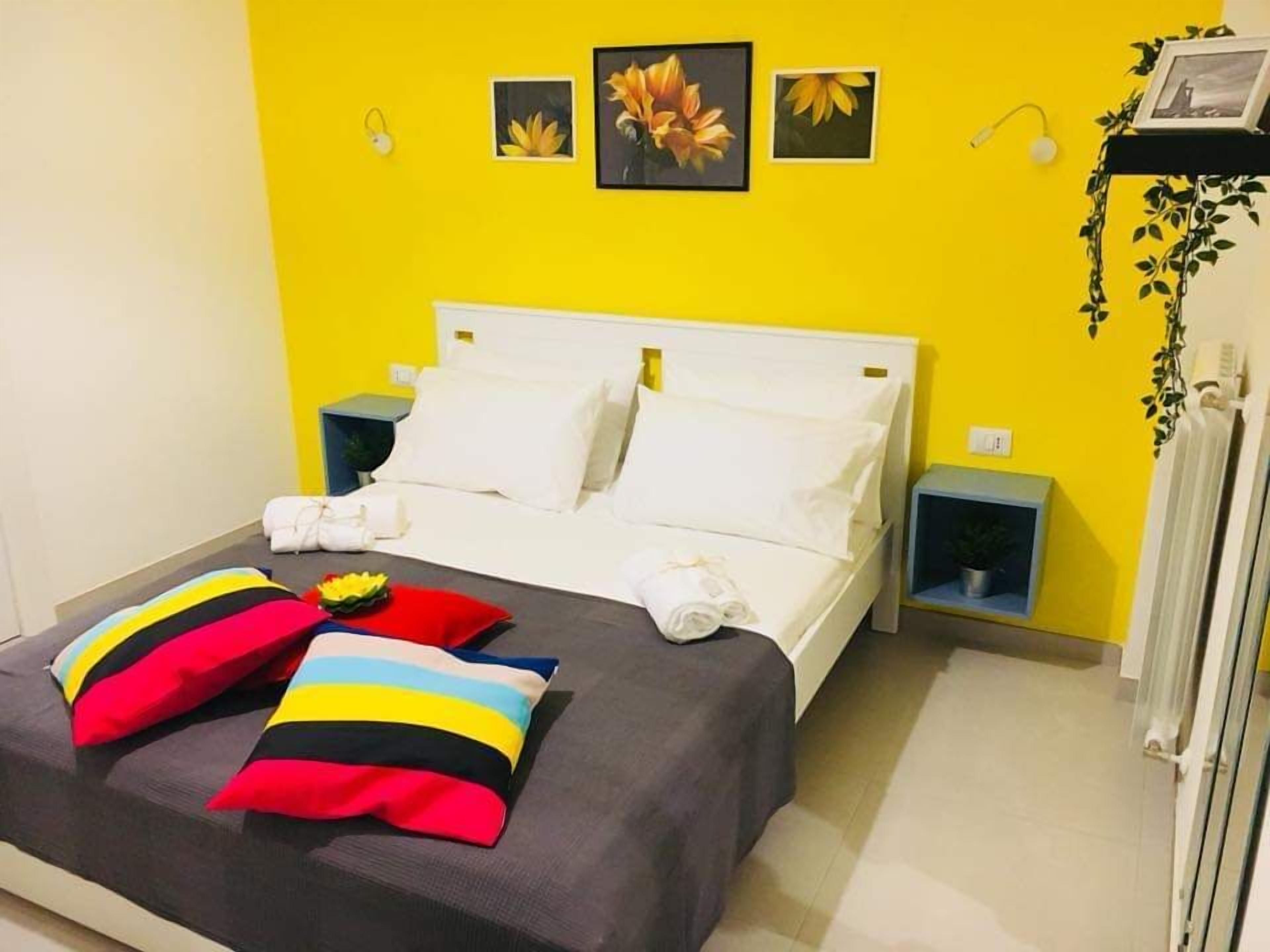 A bed with white bedding, two colorful pillows, and a small table with a plant.