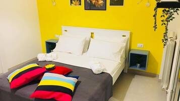 A bed with white bedding, two colorful pillows, and a small table with a plant.