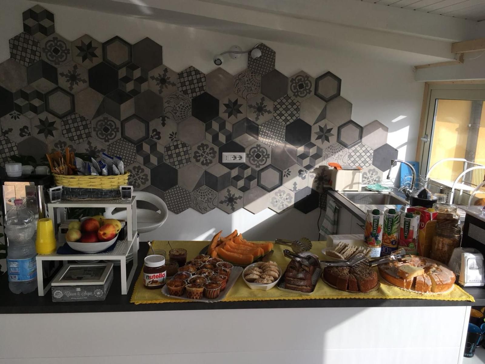 Una cocina con salpicadero de azulejos hexagonales, un frutero, una cesta de pan y diversos alimentos sobre la encimera.