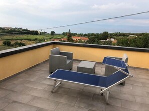 A rooftop terrace with a ping pong table, two wicker chairs, and a yellow wall. - B&B Il Giardino sul Mare (Briatico)