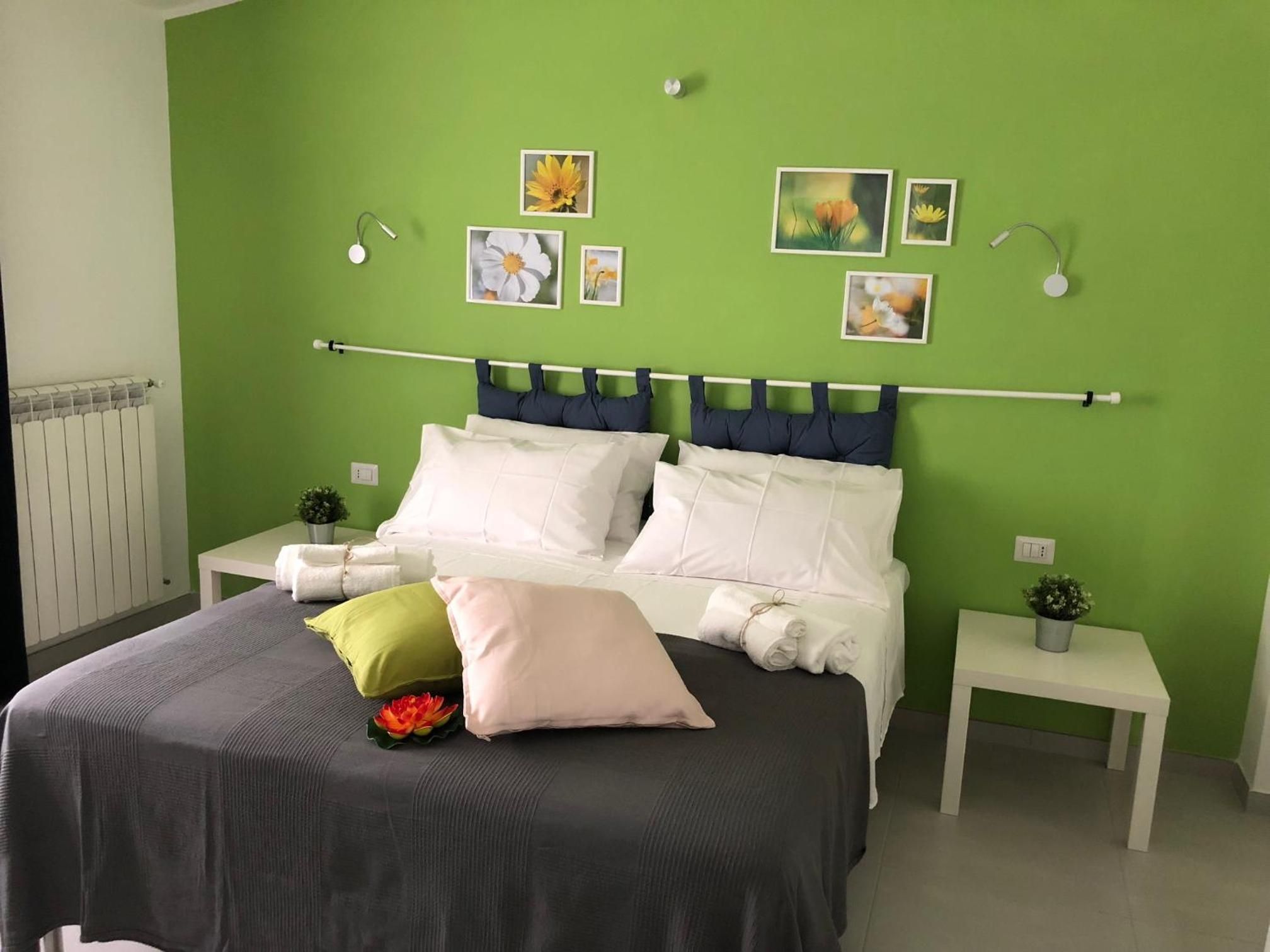 A bedroom with a green wall, a bed with white and grey bedding, and multiple framed pictures on the wall.