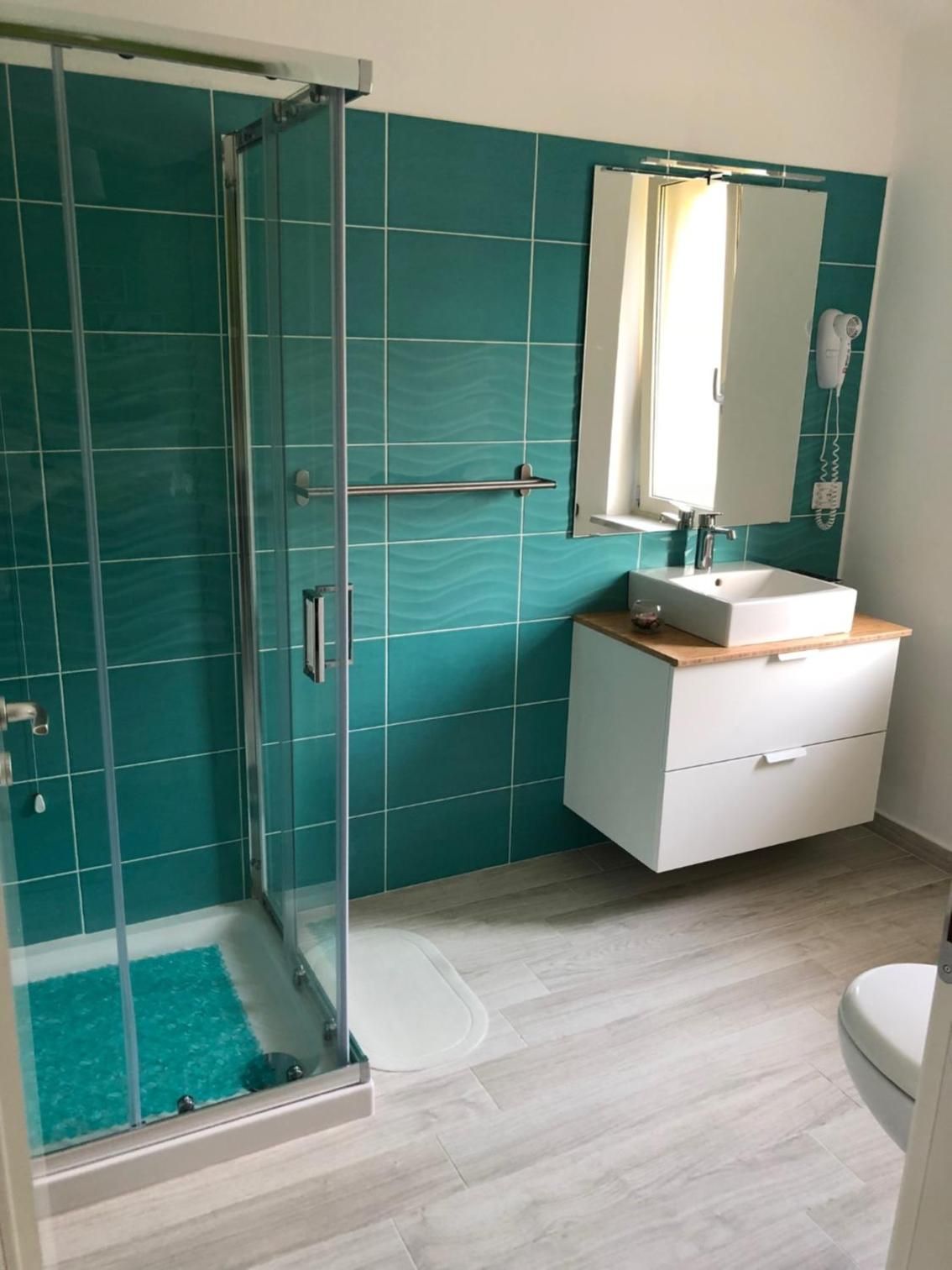 A bathroom with a glass shower enclosure, a white sink with a wooden countertop, and a mirror above the sink.
