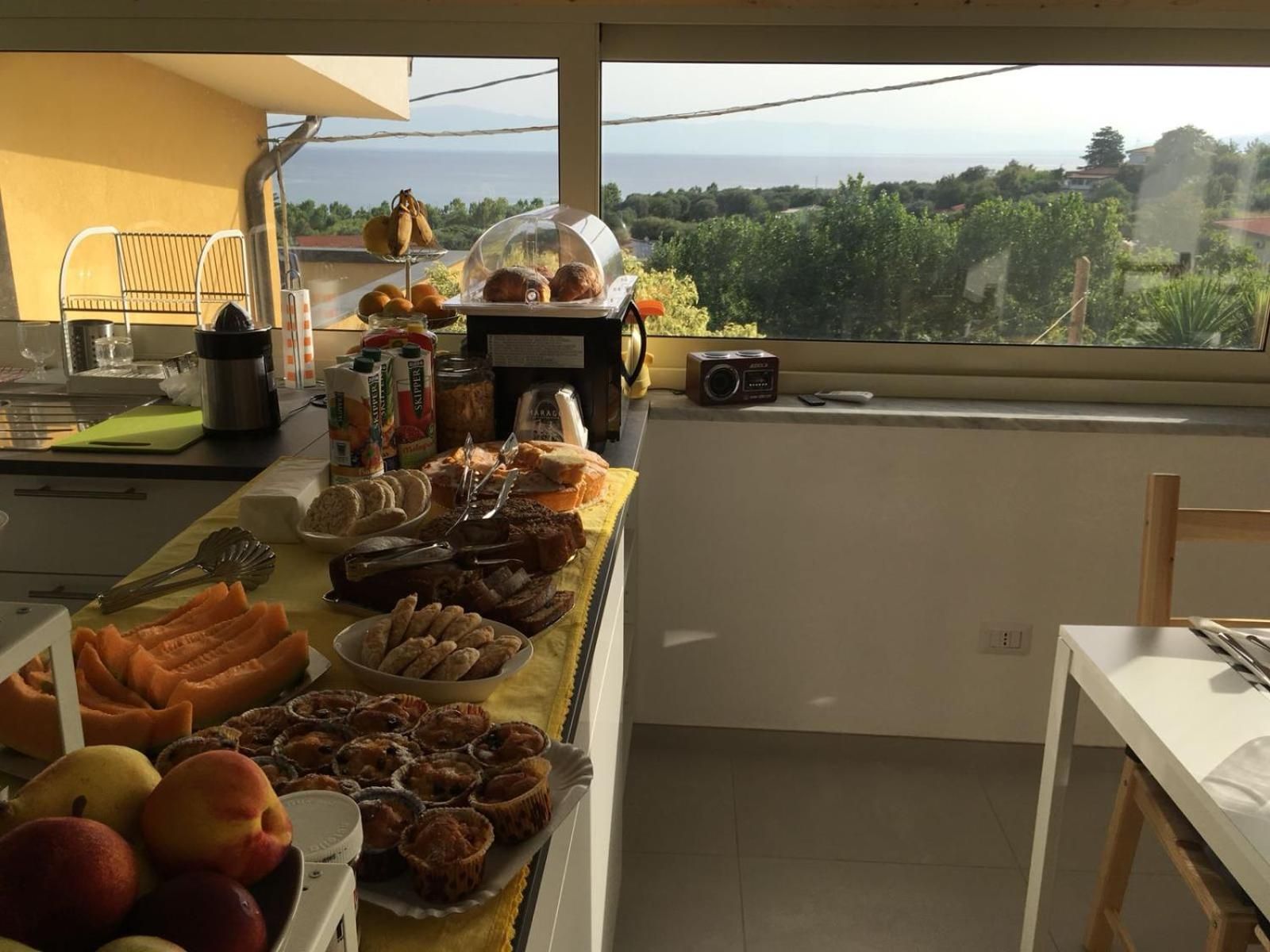 Un buffet de petit-déjeuner proposant une variété de viennoiseries, de fruits et de condiments, le tout disposé sur une table offrant une vue sur la mer.