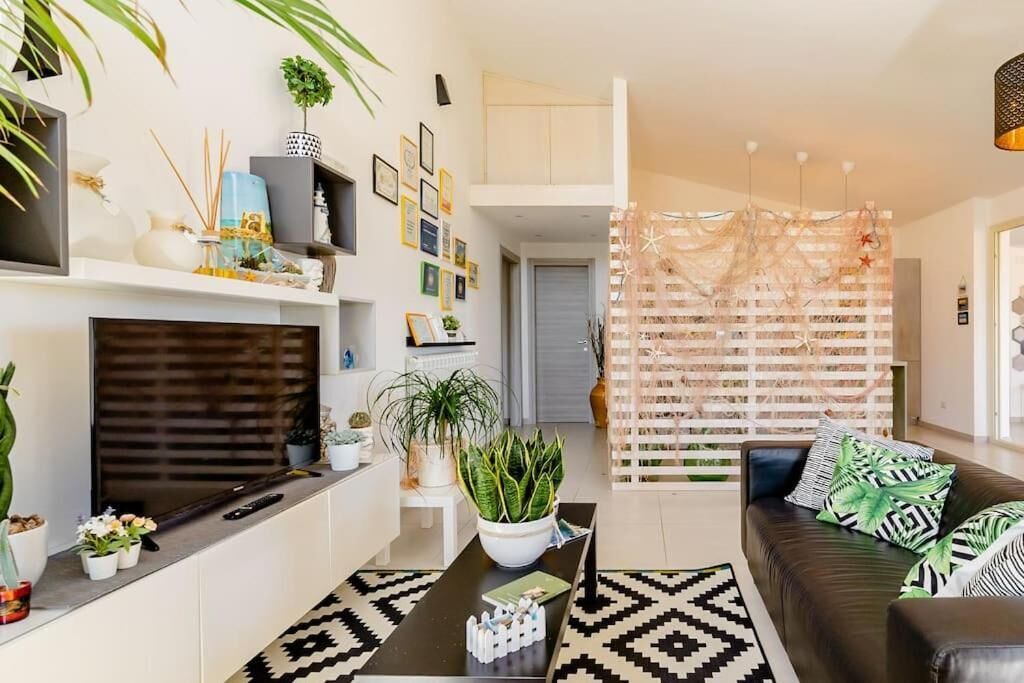 A modern living room with a fireplace, a coffee table, and a sofa. There are plants and decorative items on shelves and the coffee table.