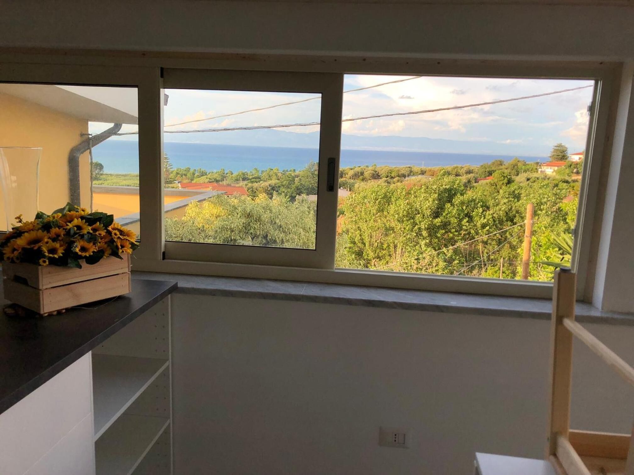 A kitchen with a large window offering a view of a vineyard and distant mountains.