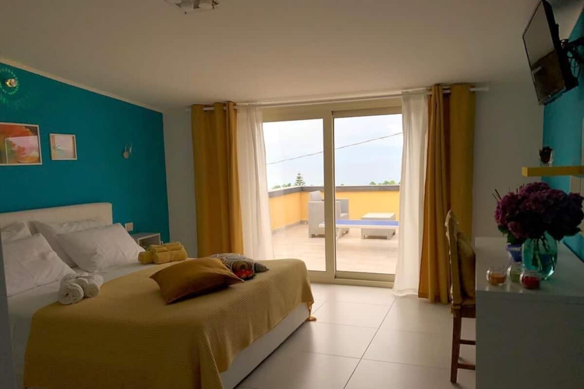 Habitación de hotel con cama, escritorio, silla, ventana con cortinas y vista al exterior.