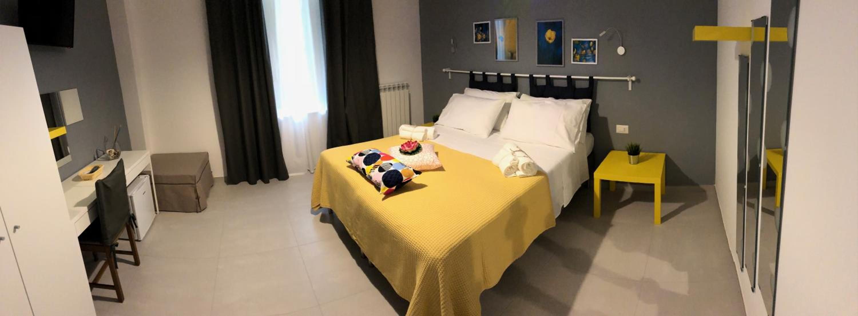 Una camera d'albergo con un letto, un comodino e una scrivania con una sedia.