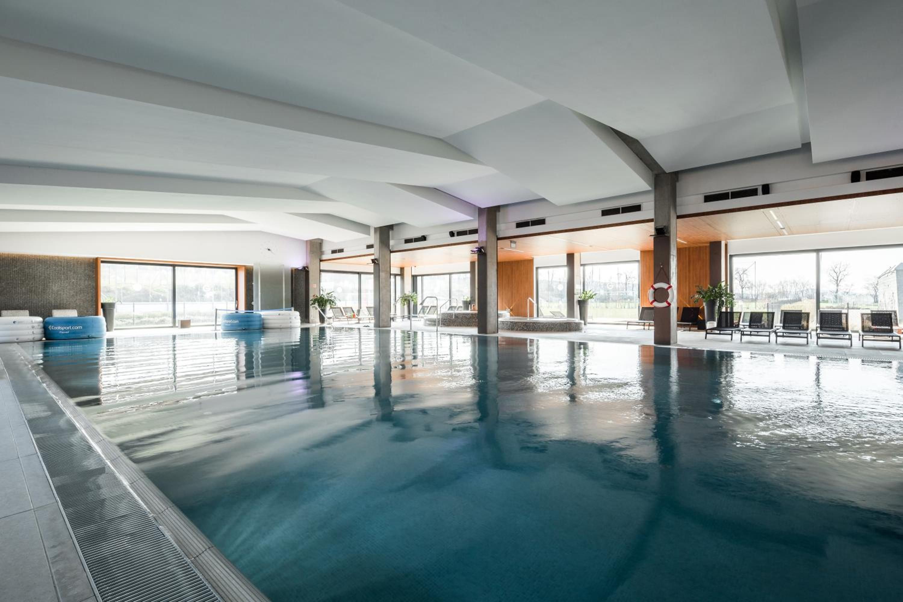 Una piscina interior con agua cristalina, sillas de descanso y amplias ventanas.