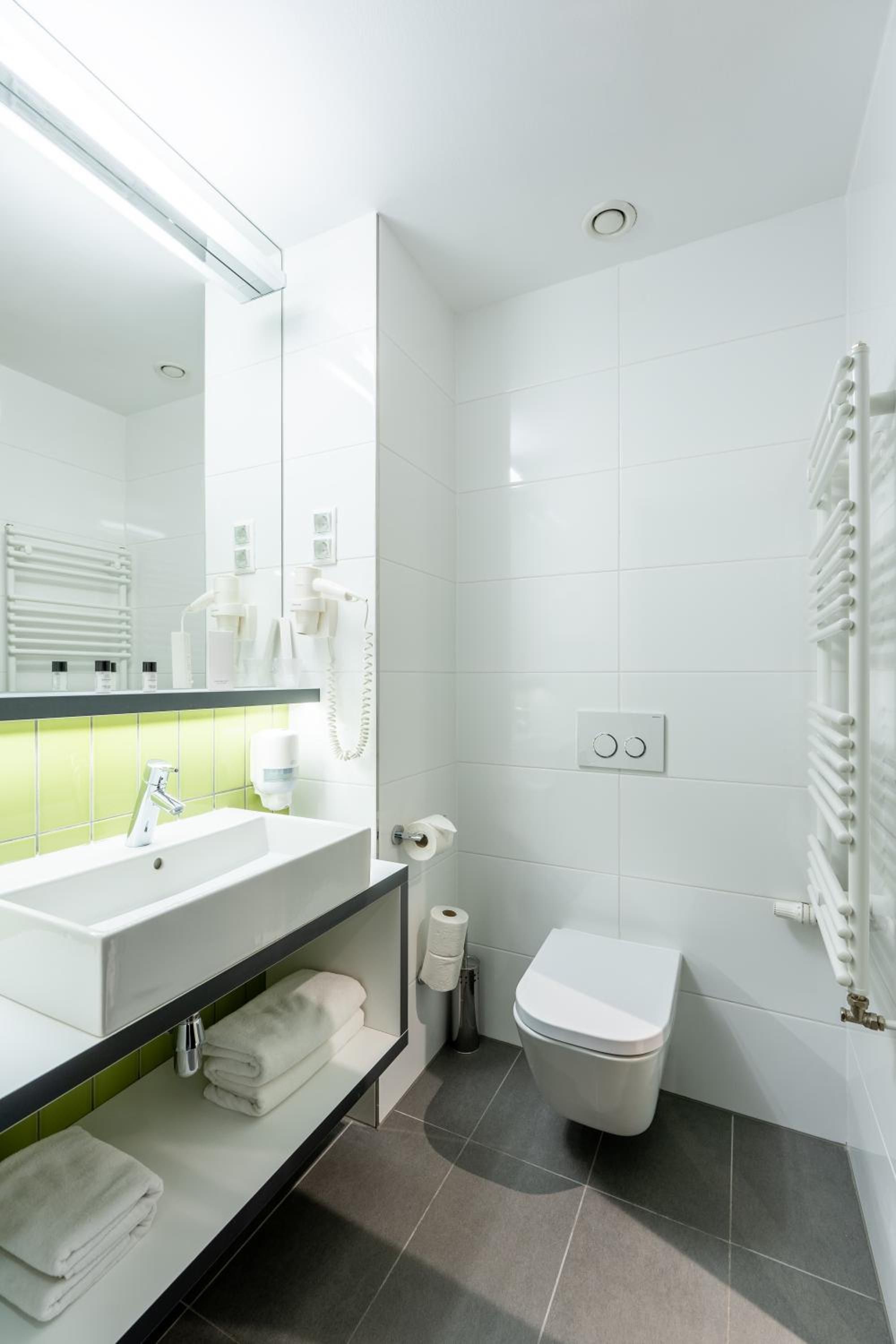 A modern bathroom with a large mirror, white fixtures, a toilet, and a towel rack.