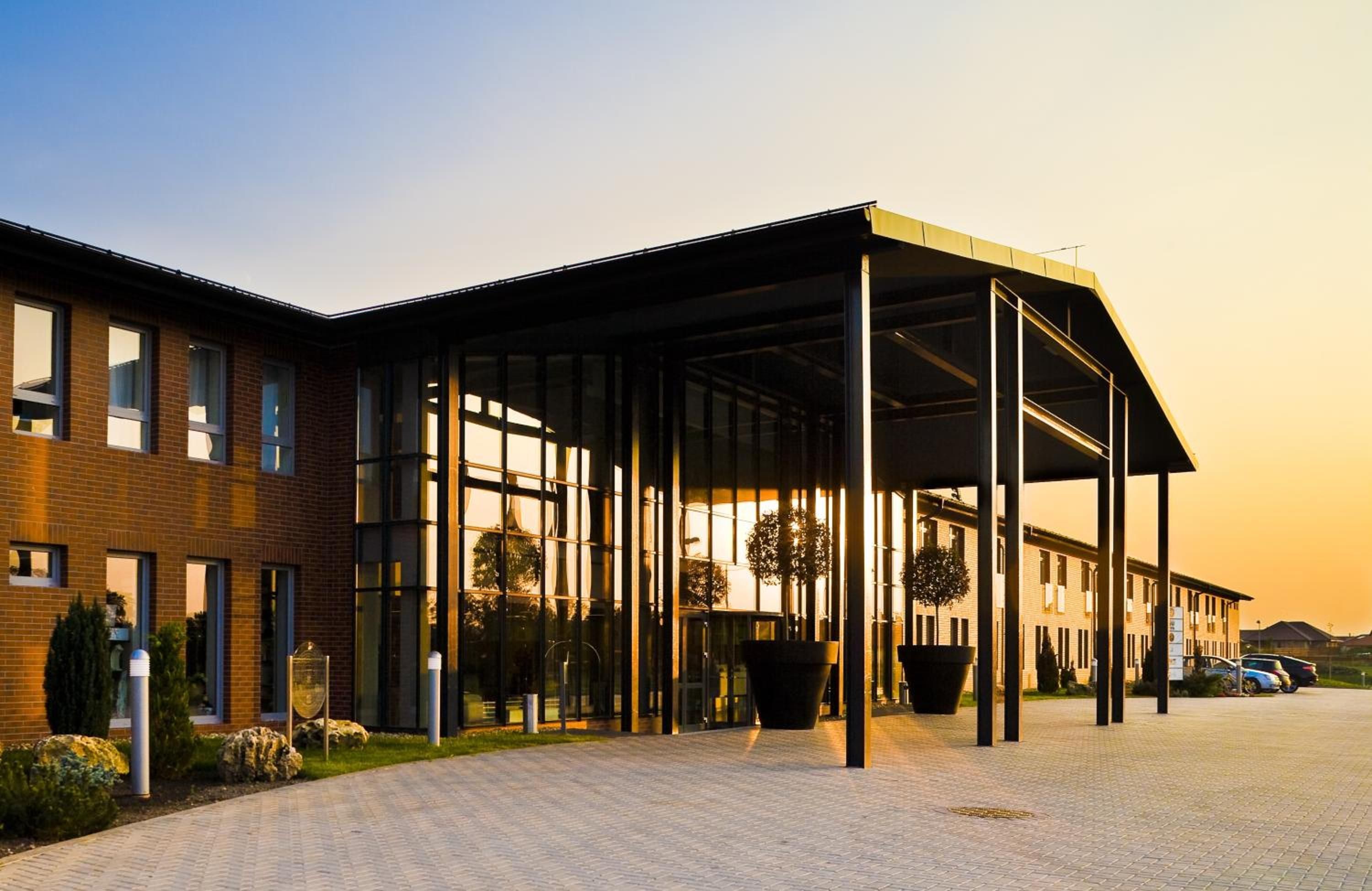 A modern building with a covered entrance, large windows, and a paved driveway.
